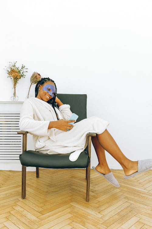 Free Young cheerful black woman relaxing with smartphone during facial treatment at home Stock Photo