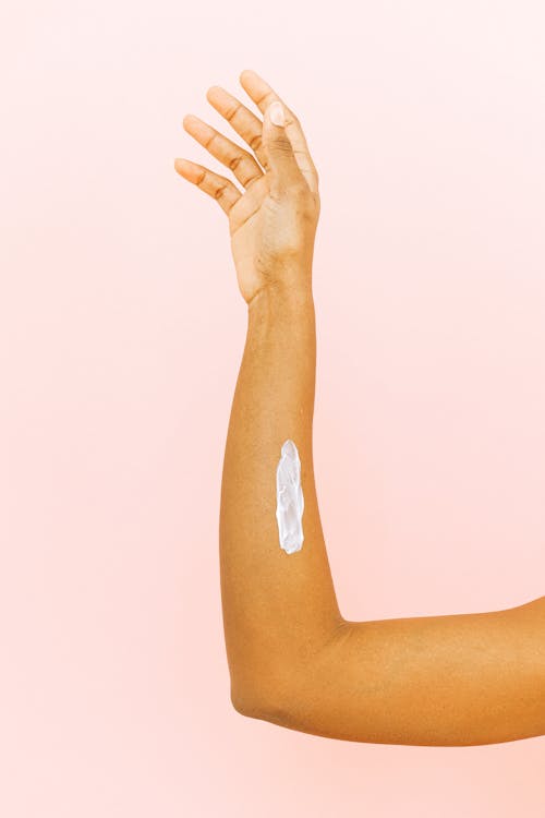 Female arm with smear for skin care against pink background