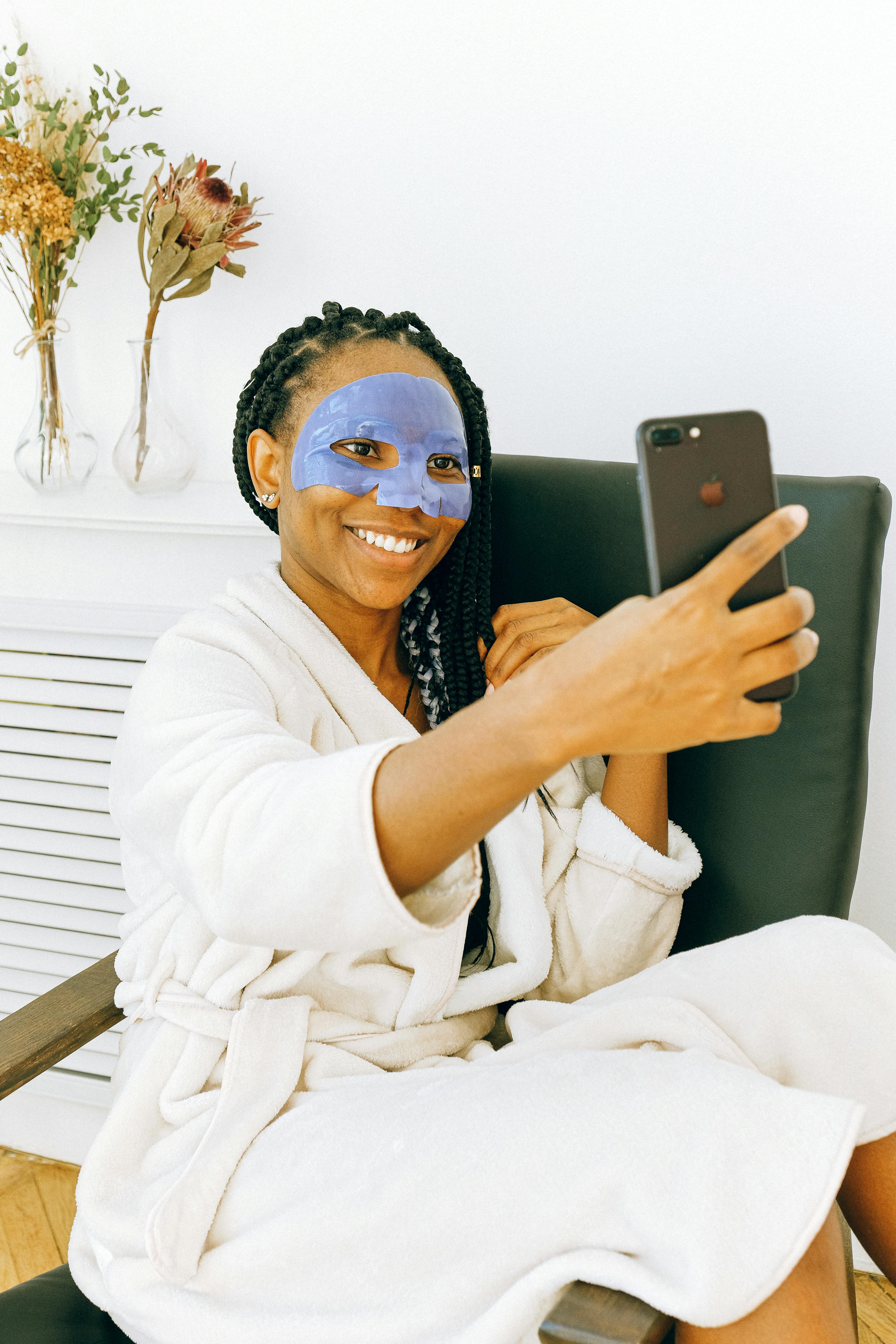 young black woman in blue facial treatment mask using smartphone at home