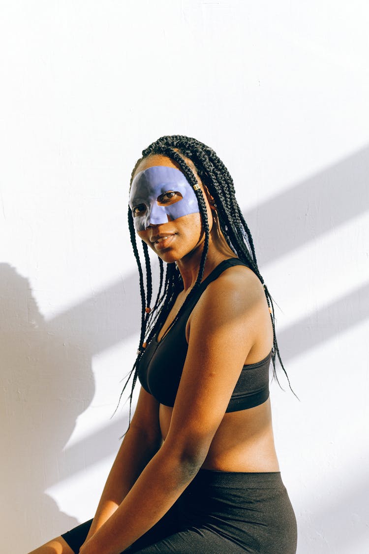 Young Black Woman In Blue Facial Treatment Mask Wearing Sportswear Near White Wall Looking At Camera