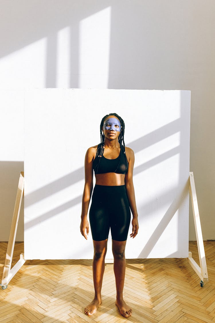 Young Black Woman In Blue Facial Treatment Mask Wearing Sportswear Against Backdrop Stand