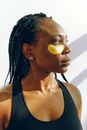 Young black woman with golden patches under eyes during cosmetic procedure