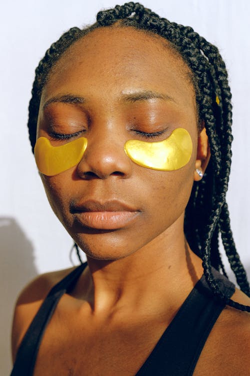 Young peaceful black woman with golden patches under eyes for grease.