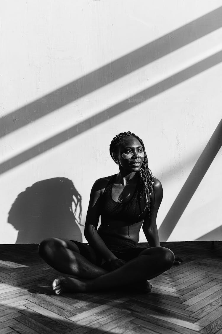 Young Satisfied Black Woman In Sportswear With Patches Under Eyes Sitting On Floor