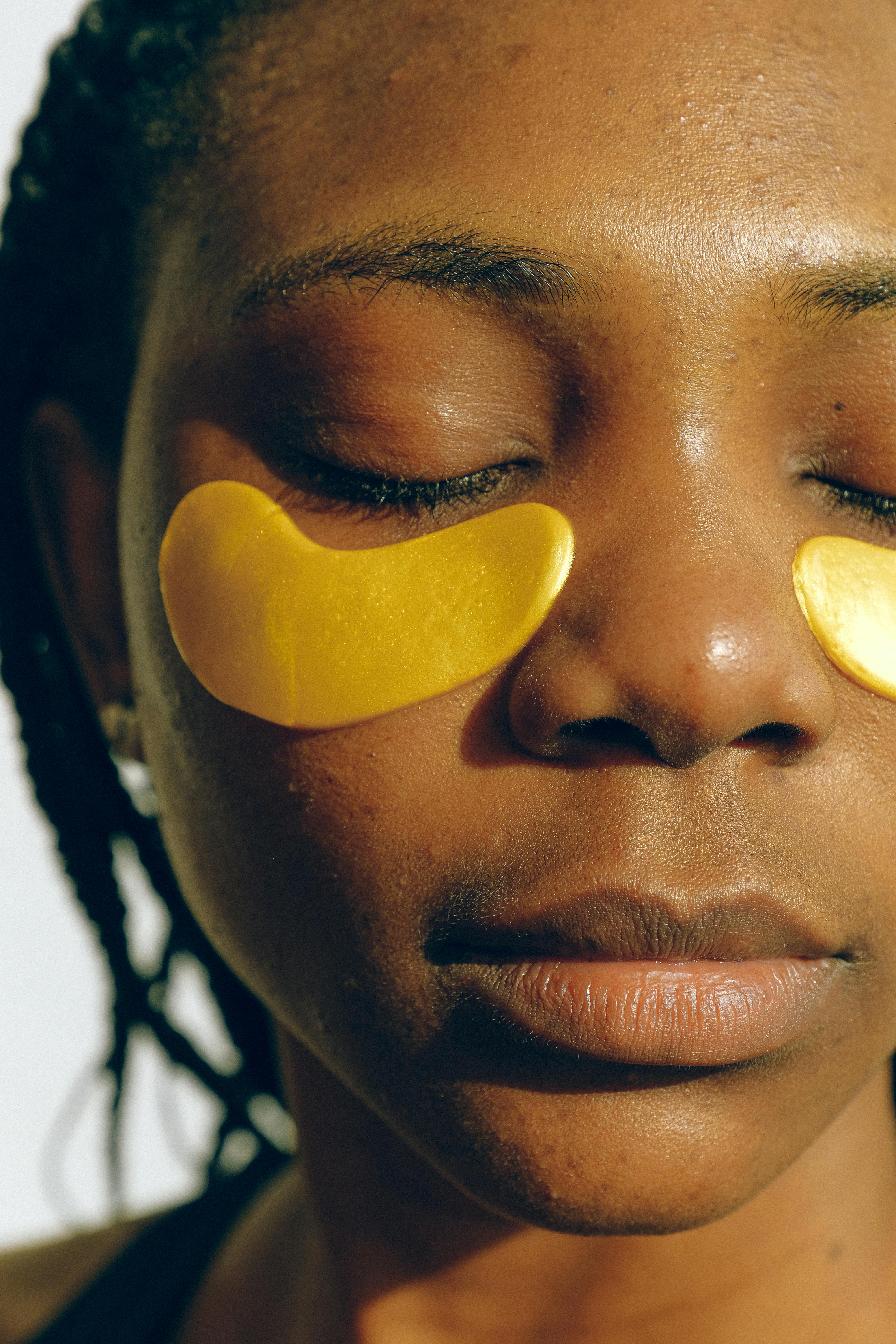 Free Crop gentle African American female with closed eyes and clean face enjoying cosmetic procedure for smoothing and moisturizing skin under eyes and removing dark circles Stock Photo