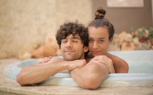 Young cheerful man and woman taking bath together enjoying holidays on blurred background of spa resort with marble interior and having romantic moments