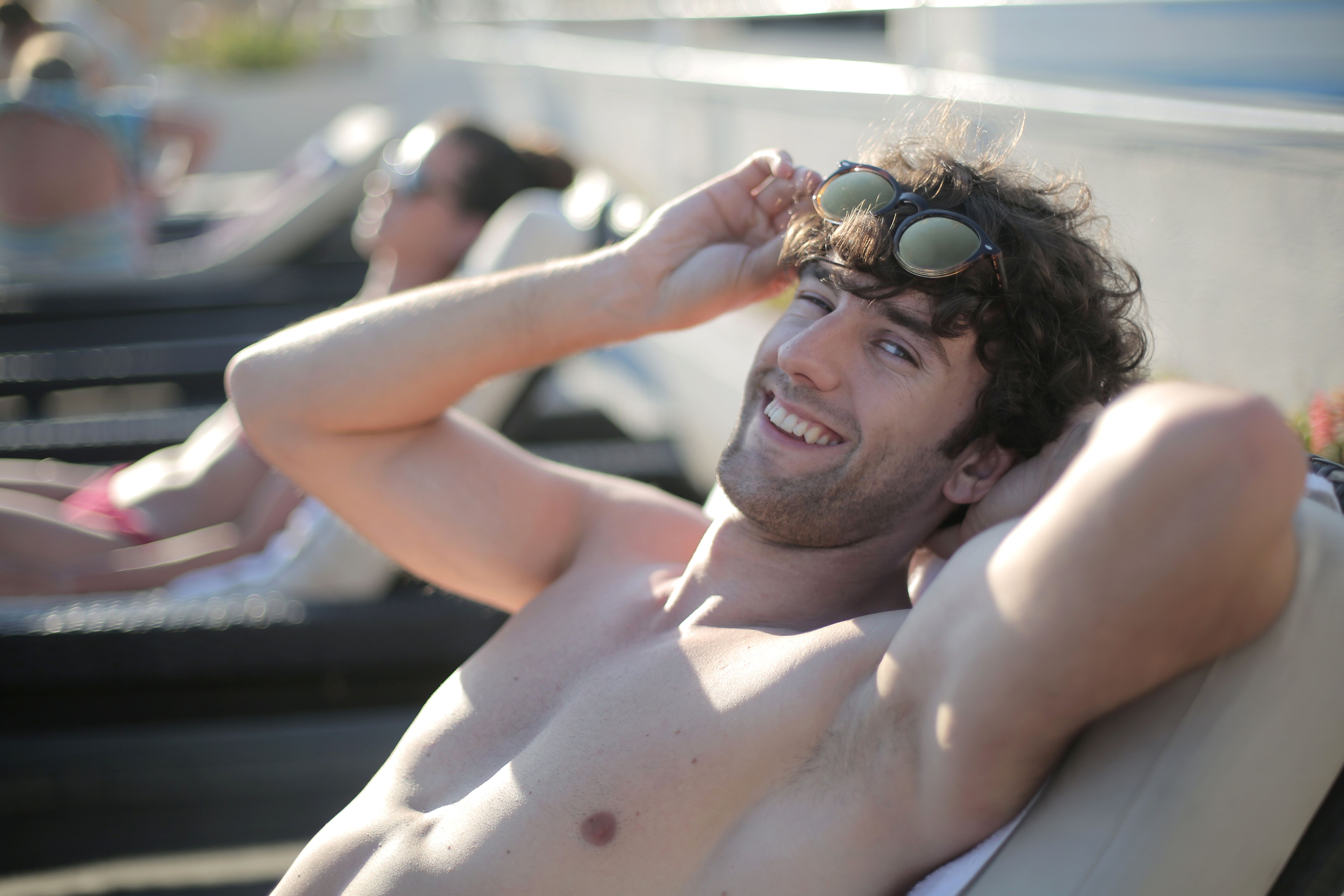 A young man enjoying a sunny day relaxing on a pool lounge chair at a resort.