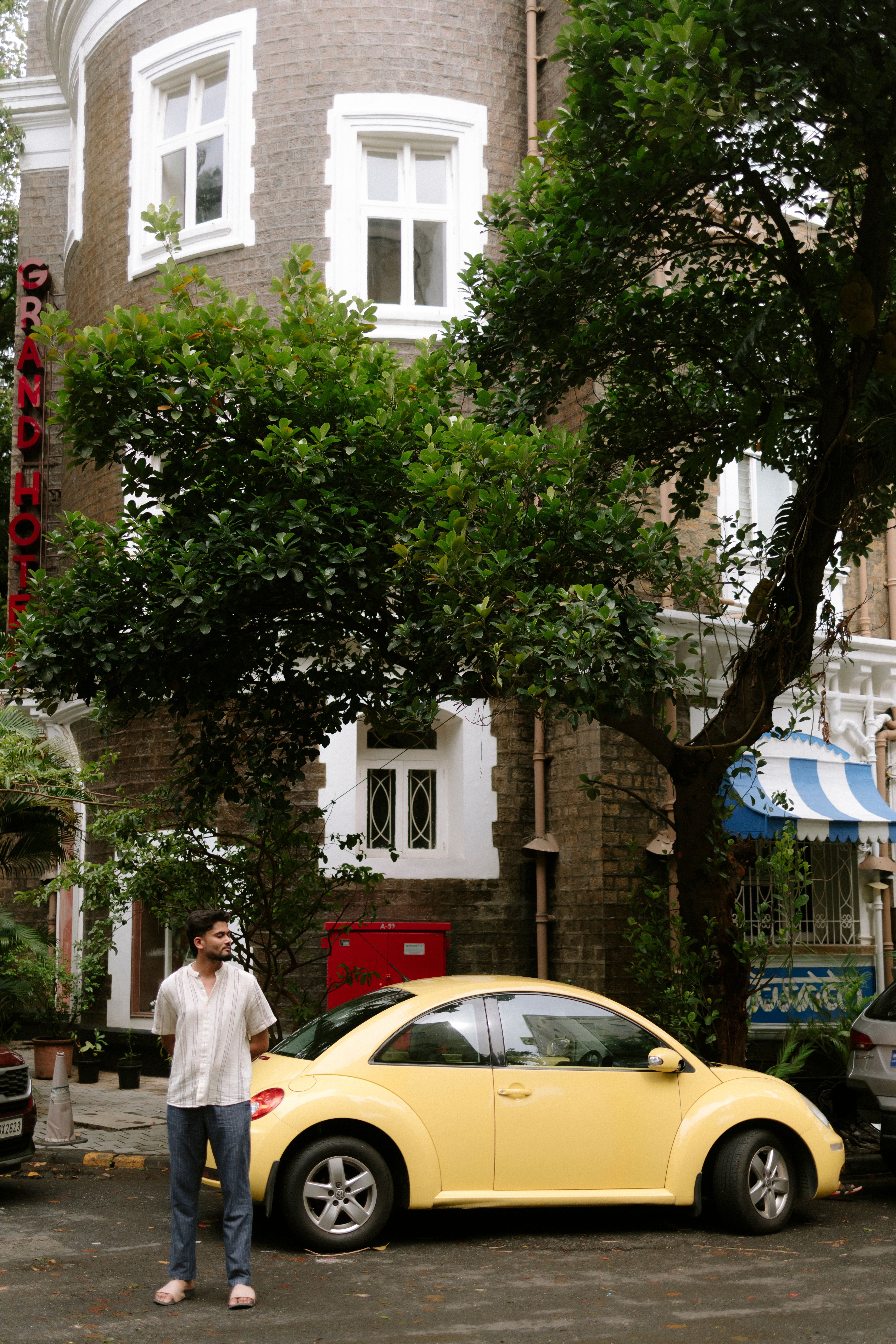 A yellow car parked near a historic building in Mumbai with lush greenery.
