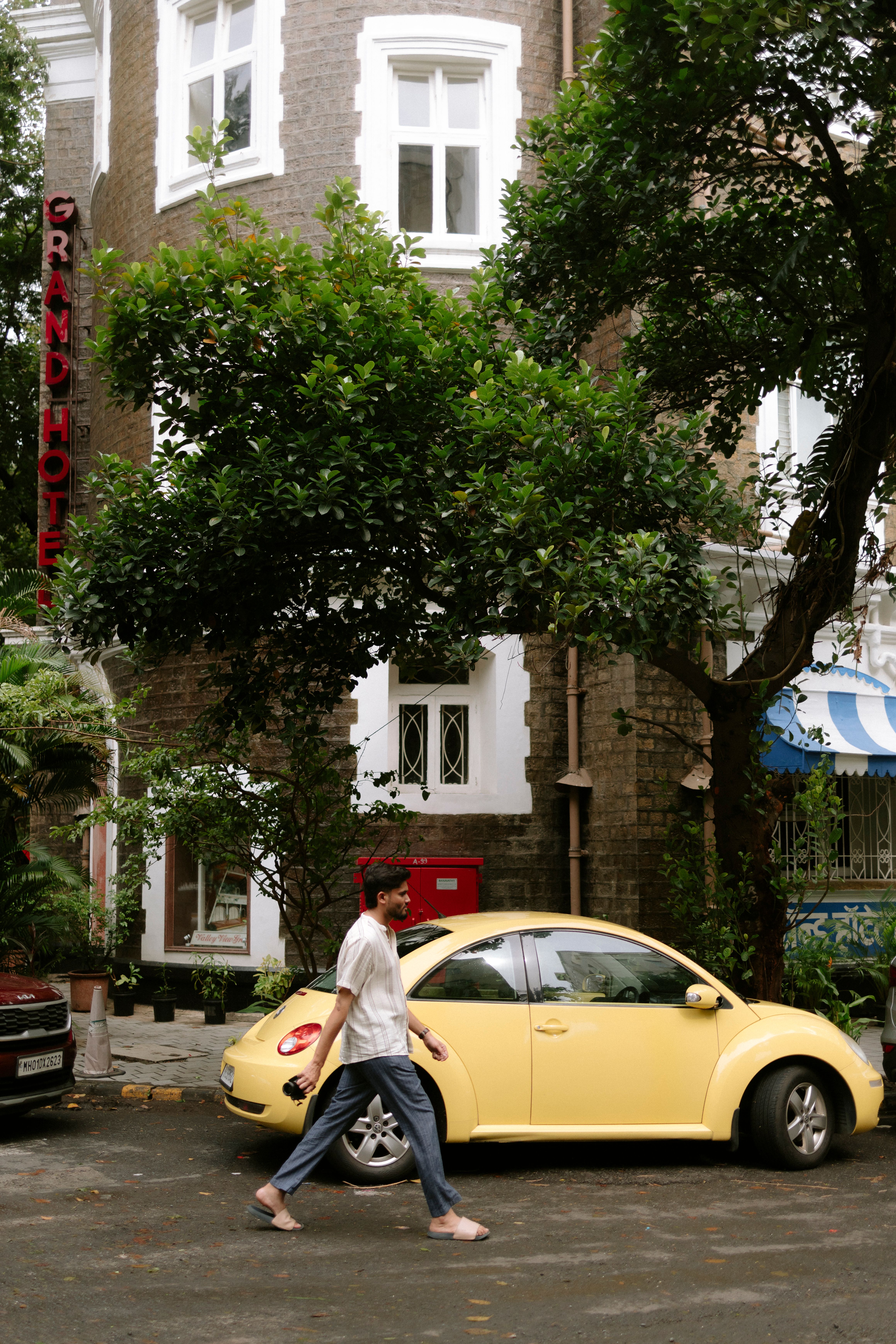 Man walking by vintage building and yellow car in Mumbai's iconic outdoor setting.