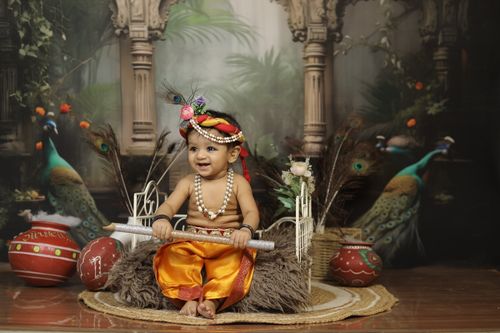 Free Adorable baby dressed as Little Krishna, surrounded by peacocks and traditional Indian decorations. Stock Photo