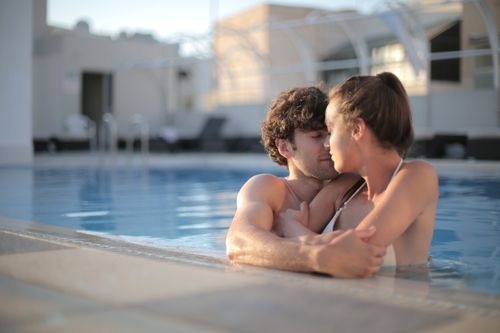Free Young couple embracing lovingly in an outdoor swimming pool on a sunny day. Stock Photo