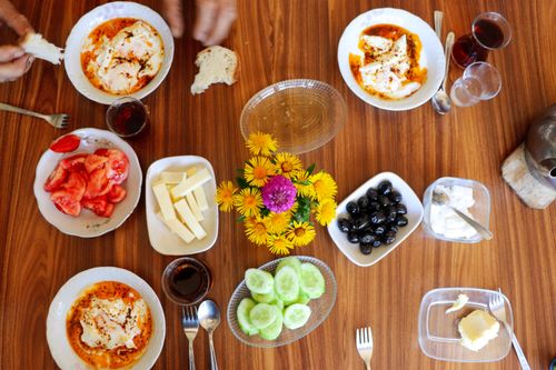Free Flat lay of a colorful breakfast with cheese, cucumbers, tomatoes, olives, and flowers on a wooden table. Stock Photo