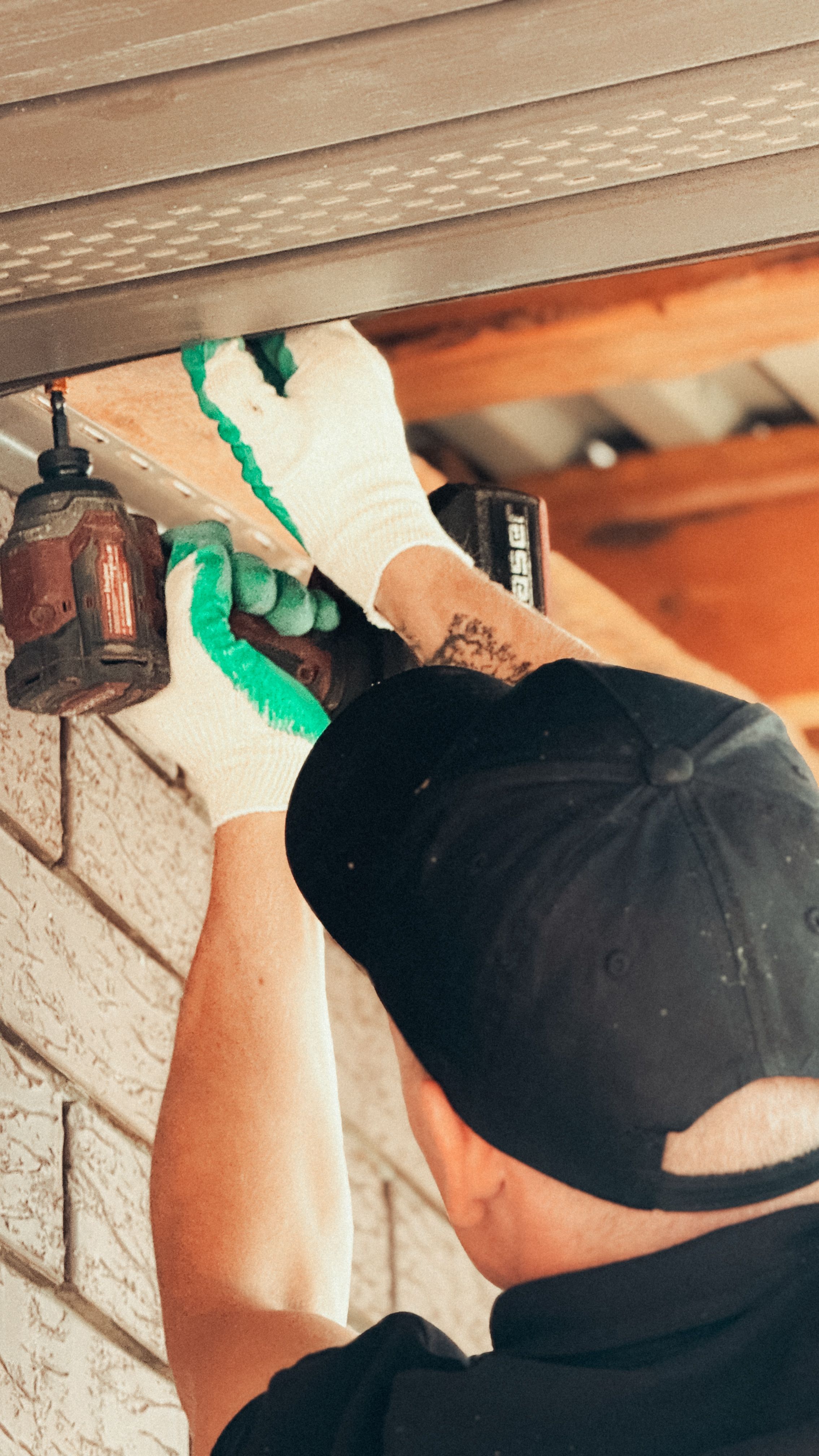 Handyman fixing an outdoor light fitting under a soffit with a cordless drill