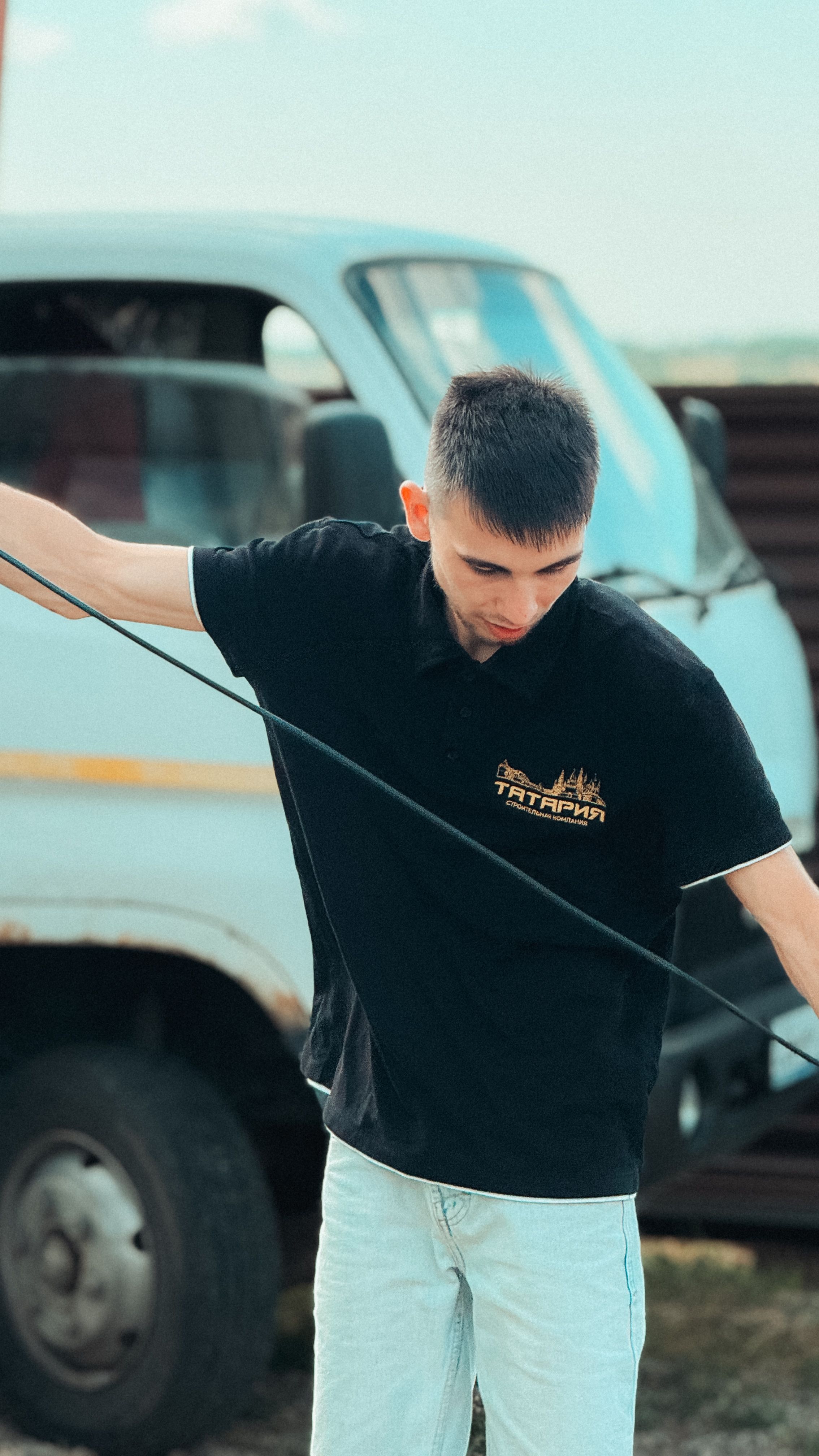 A young man adjusts equipment beside a vehicle on a sunny day, showing preparation.