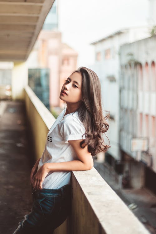 Free Woman in White Crew Neck T-shirt and Blue Denim Jeans Leaning on concrete Wall Stock Photo