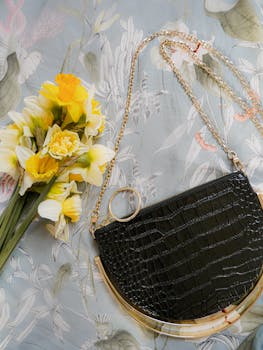 在花卉背景中，时尚的黑色手袋搭配着充满活力的黄色水仙花花束