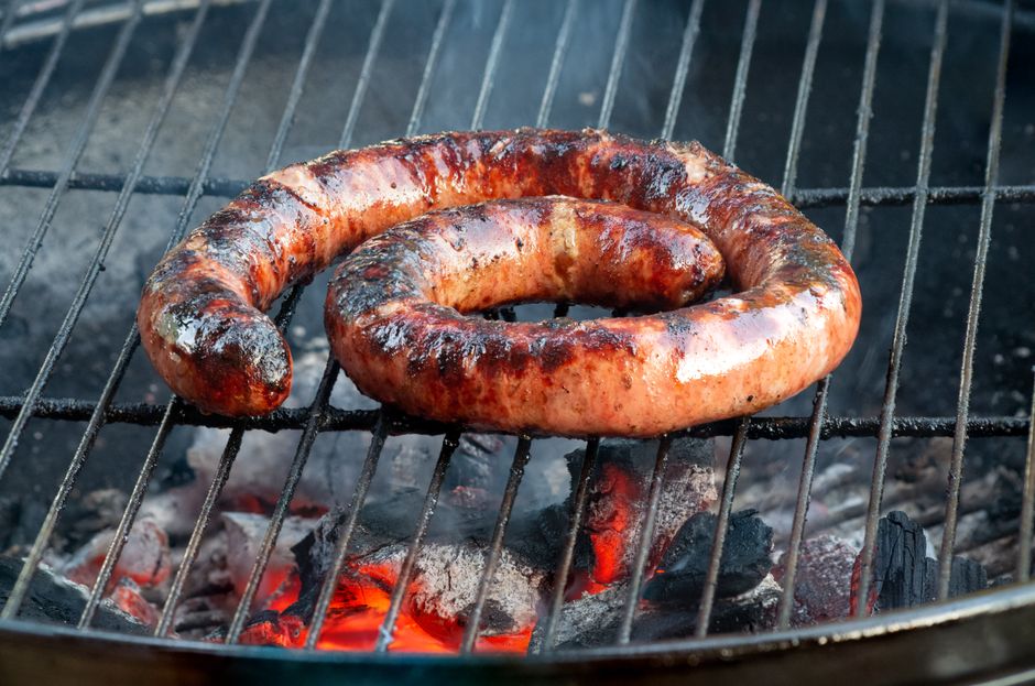 Close-up of a coiled sausage grilling over hot charcoal on a barbecue. Perfect for food and lifestyle content.