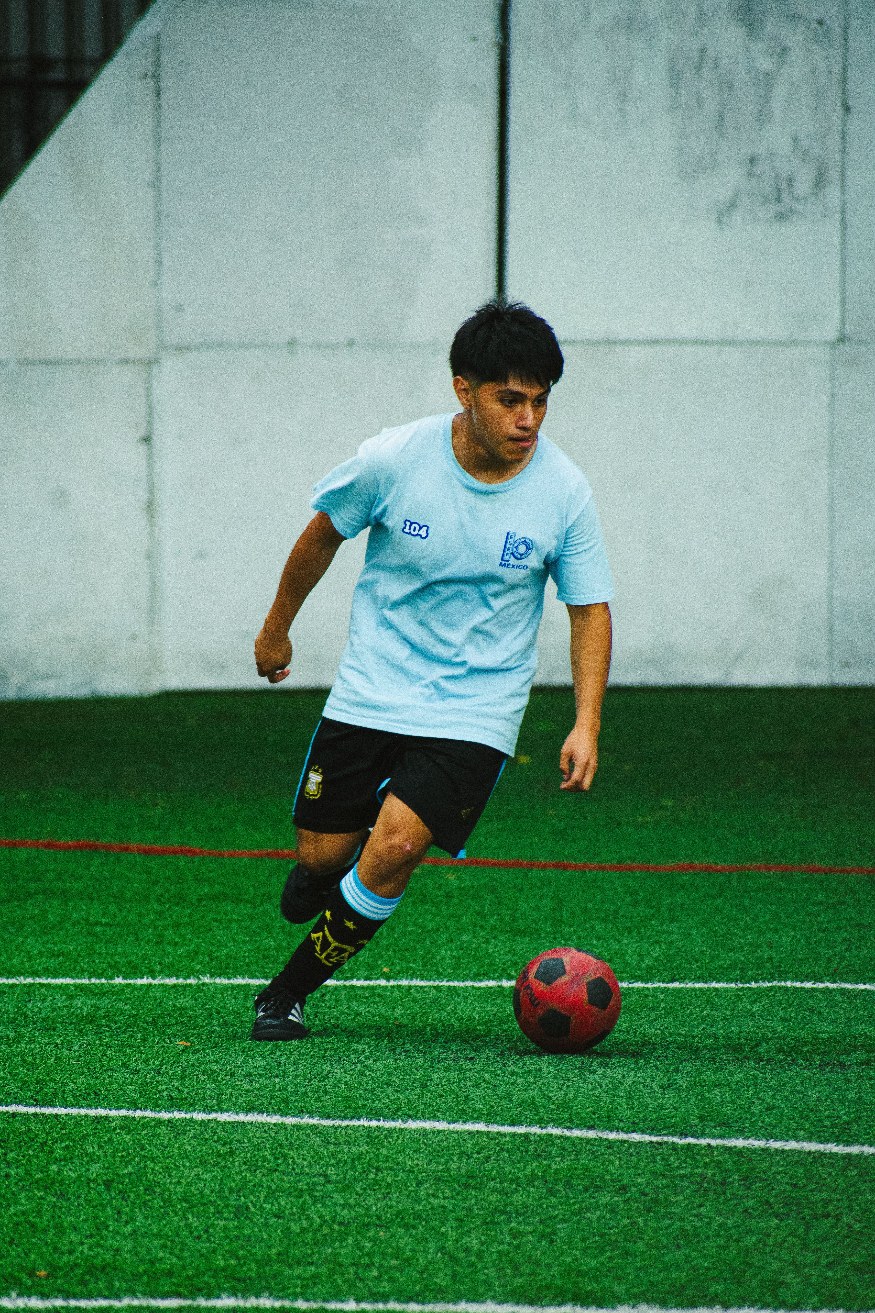 A young athlete in a light blue uniform dribbles a soccer ball on a grassy field.