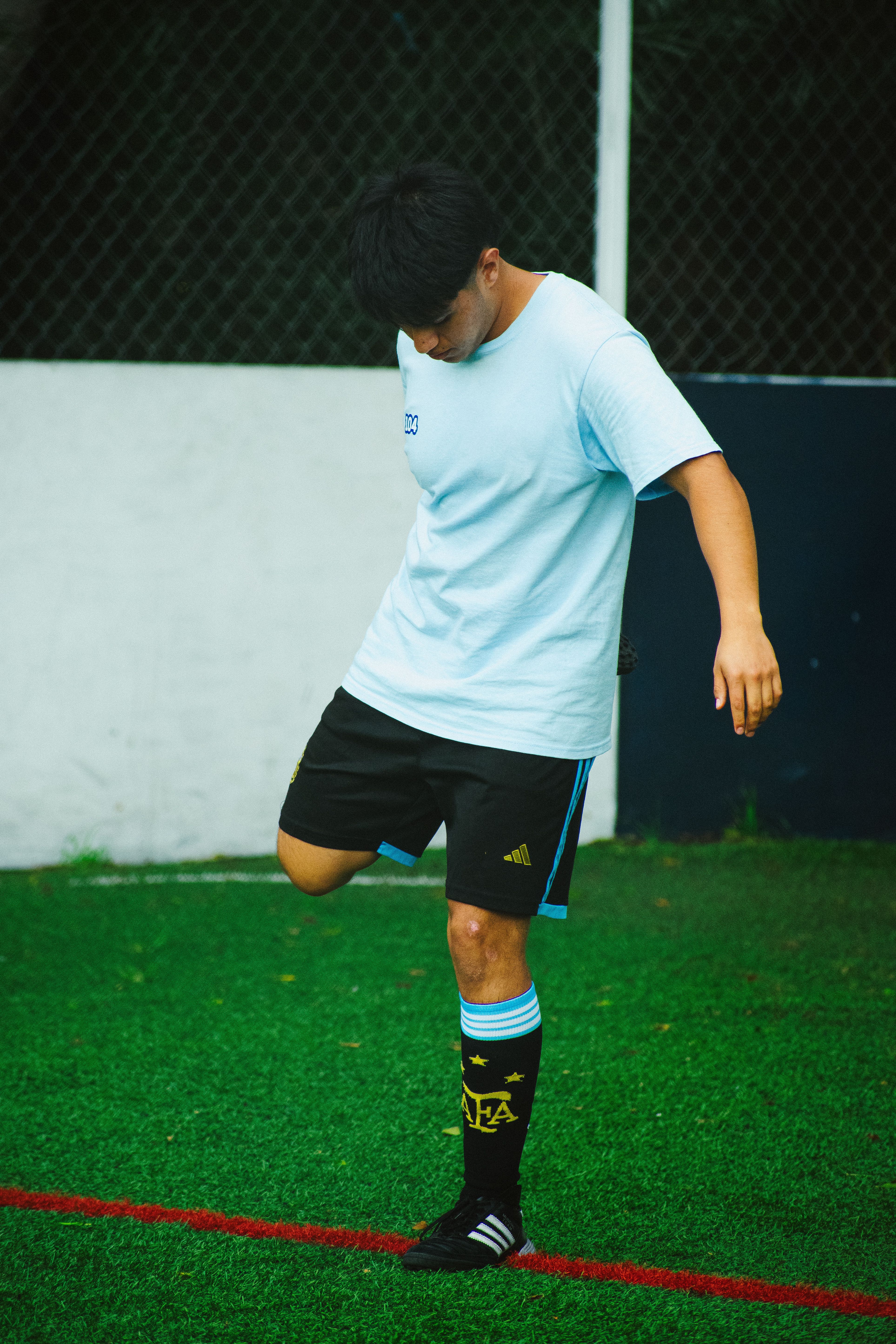 A young footballer practicing skills on a lush green field in Mexico City, wearing athletic attire.