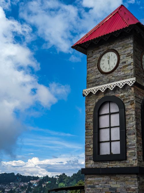 Free Stone clock tower with red roof against a bright blue sky, showcasing architectural charm. Stock Photo