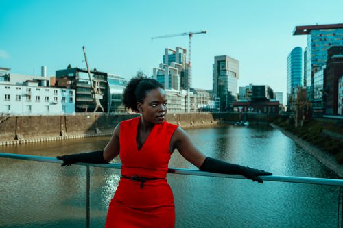 Free Stylish woman in a red dress with black gloves poses on a modern city bridge. Stock Photo