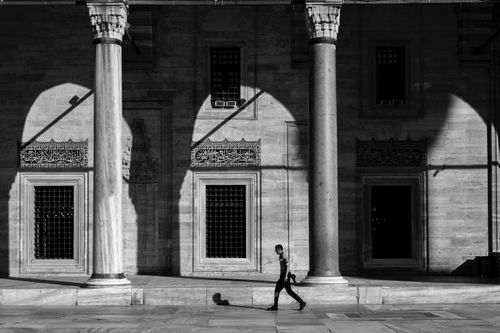 Free A lone figure walks beside historical stone columns casting dramatic shadows. Stock Photo