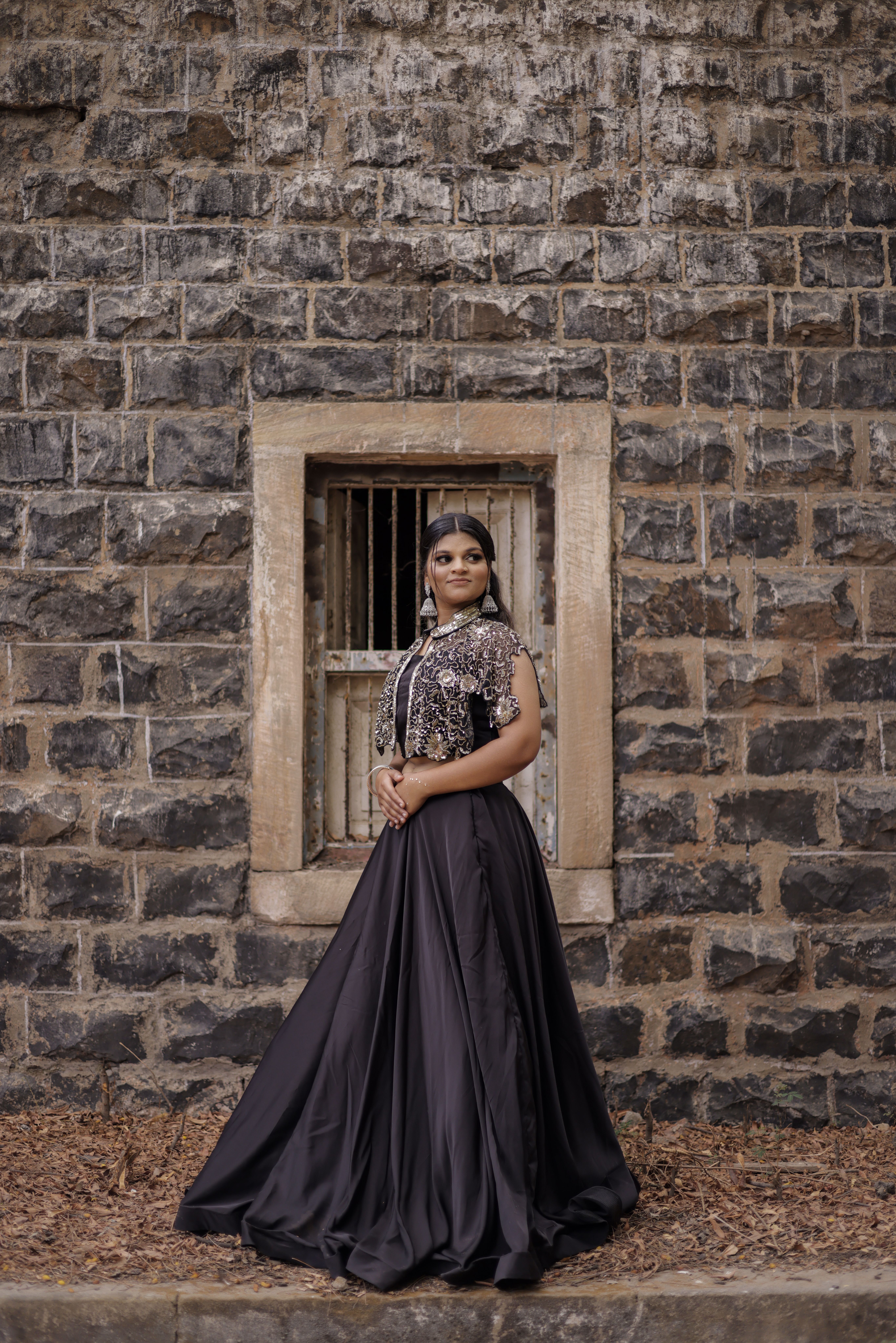 Woman in an elegant gown poses against a historic stone wall for a formal portrait.