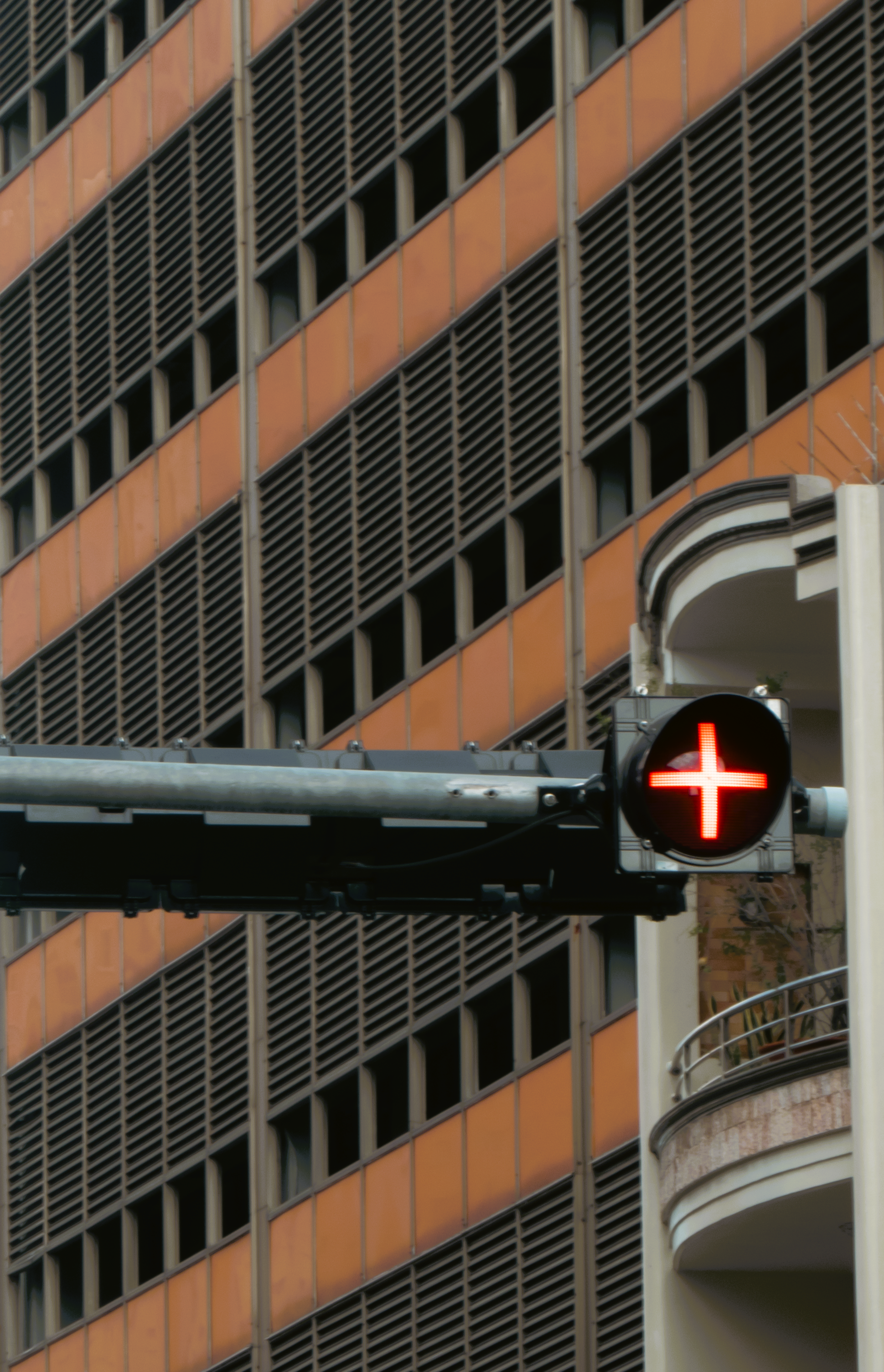 Red traffic light with cross-sign in city setting, orange building background.