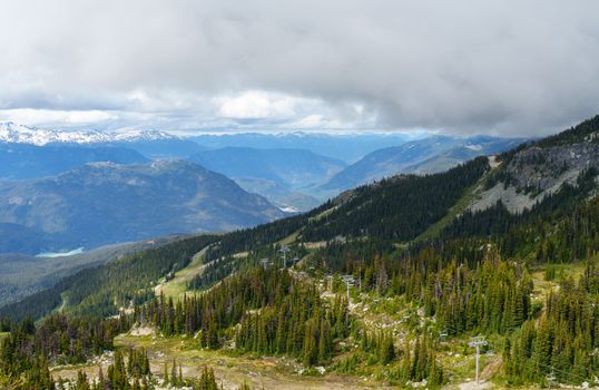 Breathtaking mountain range with lush forest under a dramatic cloudy sky.