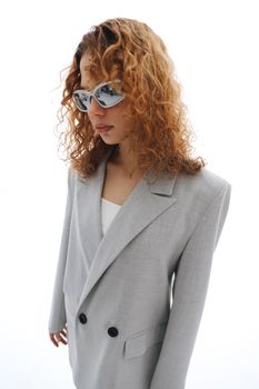 Elegant woman wearing grey blazer and sunglasses with curly hair.