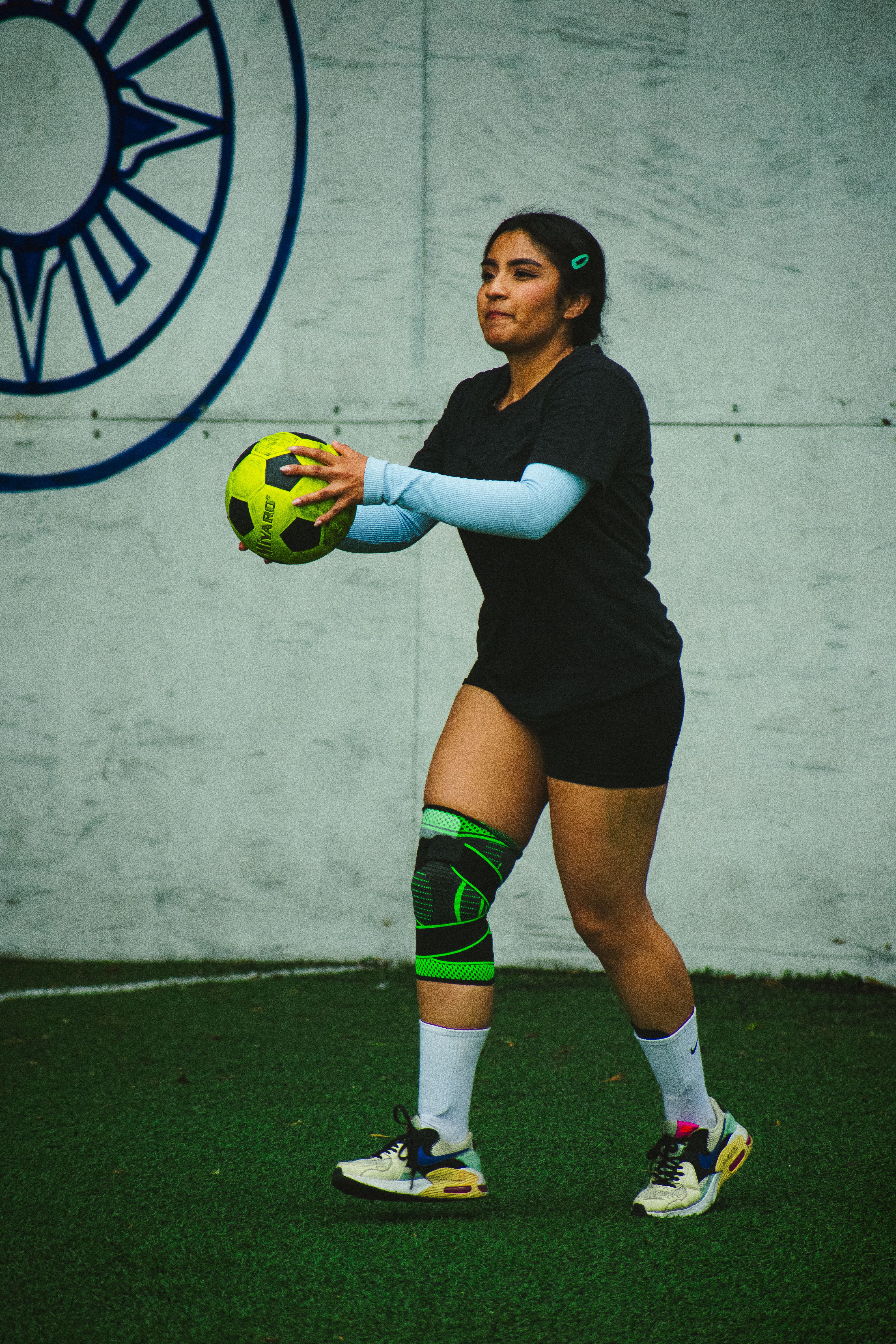 Woman in sportswear holding a soccer ball during an indoor match on a green turf field.