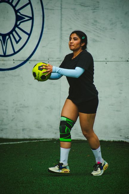 Woman in sportswear holding a soccer ball during an indoor match on a green turf field.