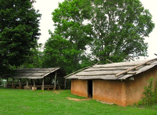Free Traditional mud hut with straw roof in a lush forest setting, surrounded by trees and natural landscape. Stock Photo