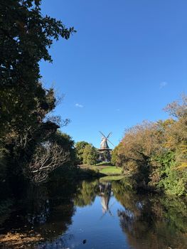 Tranquil view of a historical windmill in Bremen, Germany, reflecting in a serene lake under a clear blue sky.