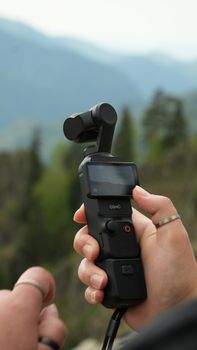 Close-up of a handheld gimbal camera with mountains in the background, ideal for travel and filming.