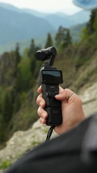 A handheld gimbal camera used by a content creator in a scenic outdoor setting.