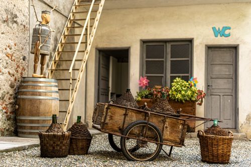 Free Vintage courtyard featuring a wooden cart, wicker baskets, and barrels against a rustic building. Stock Photo