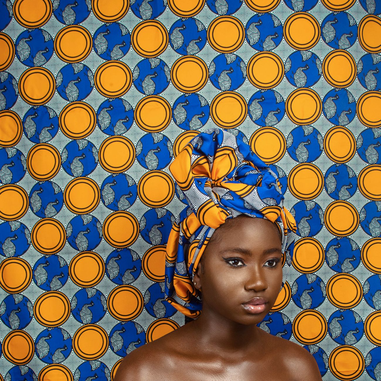 Elegant portrait of a woman wearing a vibrant African head wrap against a patterned background in Lagos, Nigeria.
