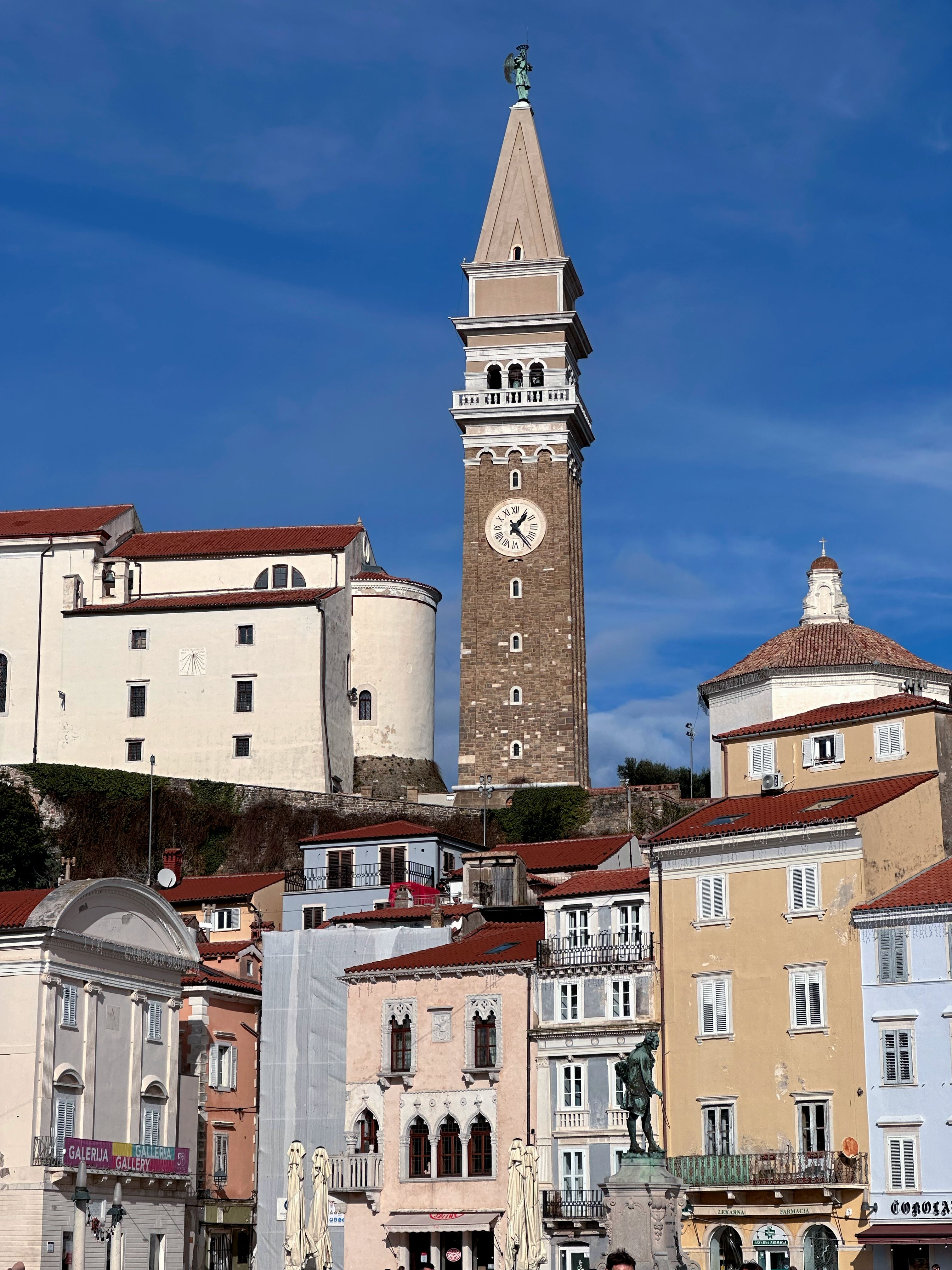 Beautiful view of Piran's iconic bell tower against a clear blue sky, surrounded by colorful buildings.