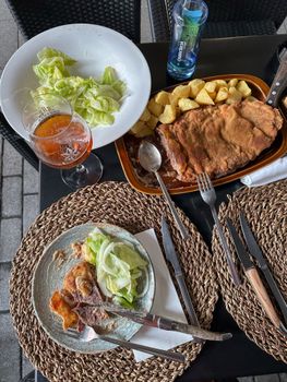 Delicious breaded meat with potatoes, salad, and beer on an outdoor terrace.