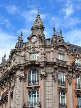 Beautiful baroque-style building facade with clock in Gijón, Spain under blue sky.