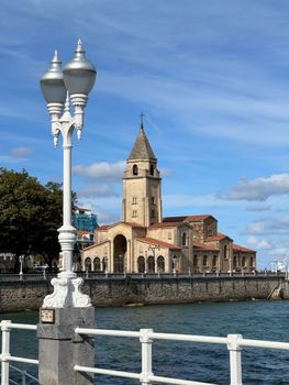 Historic Iglesia de San Pedro in Gijón, Spain, captured with a foreground lamp post under a blue sky.