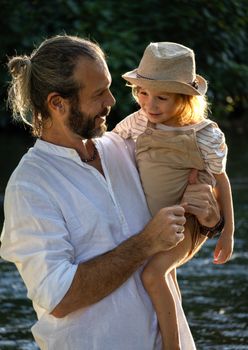 Father holding his smiling child by a river, conveying love and joy.