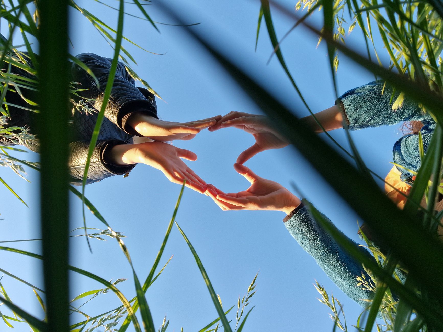 A unique perspective of hands forming a heart shape against a blue sky.