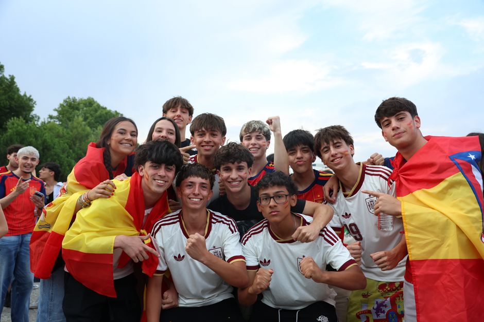 Un grupo alegre de jóvenes celebra al aire libre, mostrando con orgullo banderas españolas y camisetas de equipo.