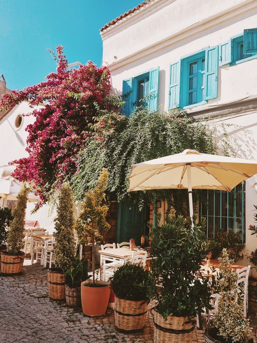 Free Outdoor cafe with flowers and umbrellas in Bozcaada, Türkiye, showcasing Mediterranean charm. Stock Photo