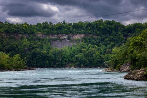 Free Expansive view of a river lined by dense forests under a dramatic cloudy sky. Stock Photo