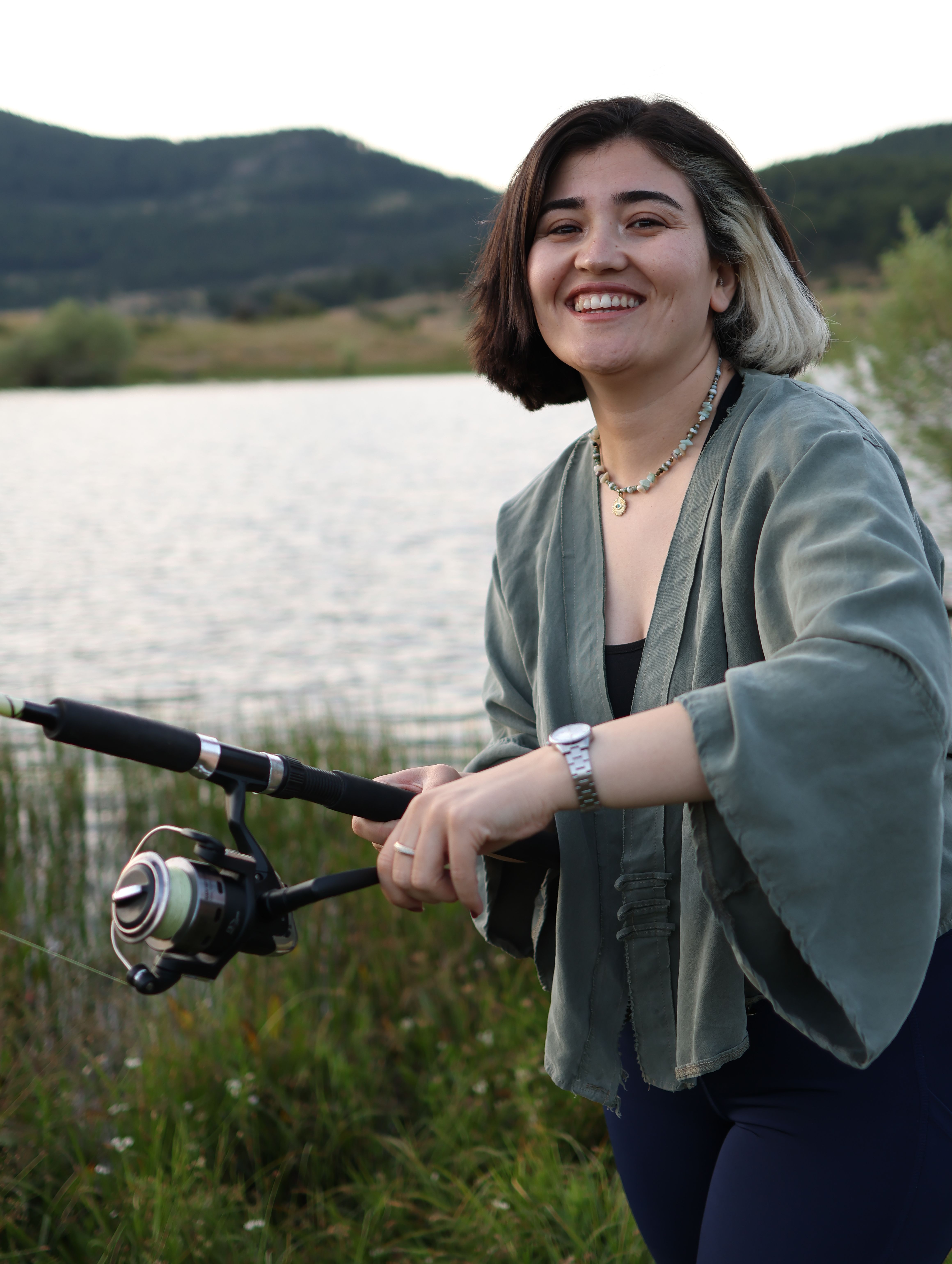 Happy young woman fishing by the serene lake during a beautiful day outdoors.