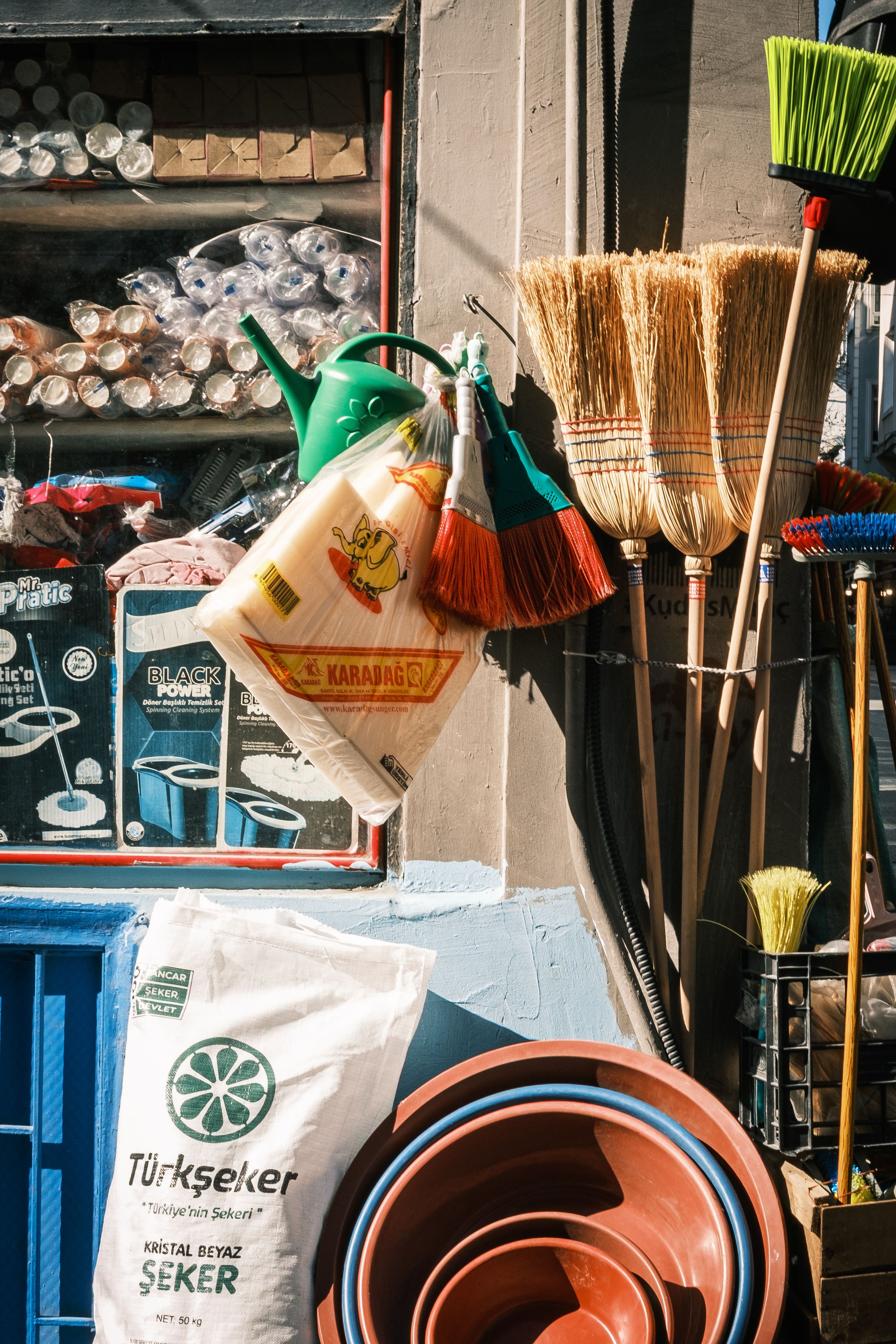 Local market stall showcasing brooms, buckets, and sugar sacks in vibrant sunlight.