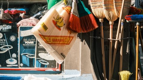 Local market stall showcasing brooms, buckets, and sugar sacks in vibrant sunlight.